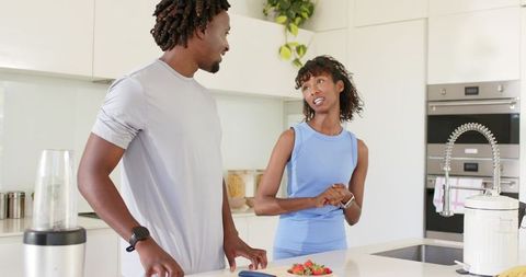 African couple in sportswear chatting at kitchen island with blender and strawberries