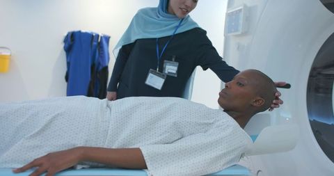African american patient receiving ct scan while technician in hijab positioning headrest