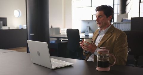 Businessperson Using Laptop Multitasking with Coffee in Office