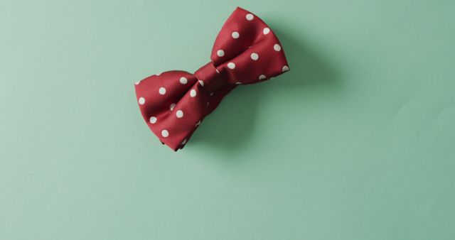 Red polka dot bow tie placed on a mint green background, creating a striking contrast. Ideal for websites, blogs, or articles related to men's fashion, formal accessories, and classic style. Can be used for fashion catalogs, product advertisements, or social media graphics emphasizing elegance and simplicity.