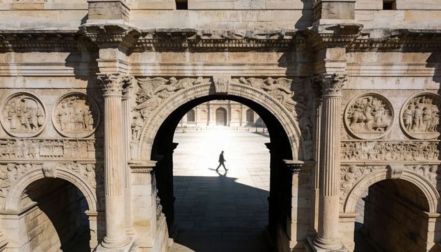 Solitary pedestrian walking through ornate ancient arch with strong sunlight and shadow