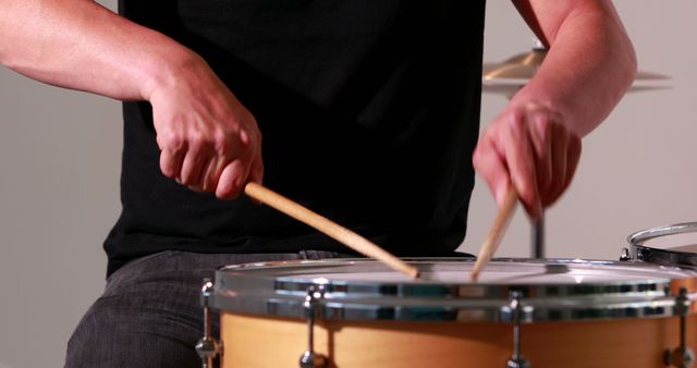 Close-up of person playing drum with wooden drumsticks. Focus on hands and drum, creating dynamic scene of percussion performance. Ideal for use in materials related to music education, percussion instruments, musicians in action, and live music performances.