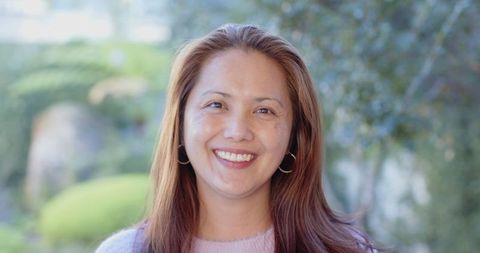 Smiling asian woman in garden with gold hoop earrings and sweater