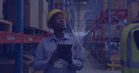 Black Warehouse Manager Inspecting Inventory with Tablet and Hard Hat in Aisle