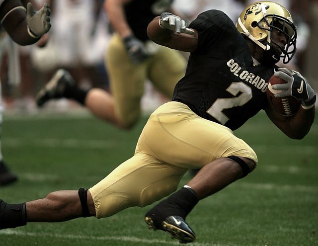 American football player in black and gold running with ball during a game. Ideal for sports magazines, fitness promotions, team spirit campaigns, and advertisements related to athletic products.