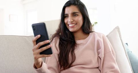 Smiling Indian Woman Relaxing on Couch with Smartphone