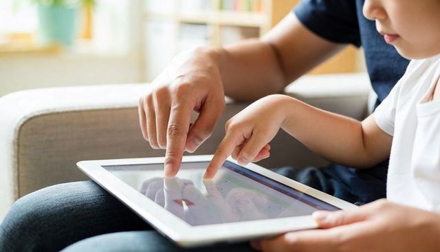 Parent and Child Sharing White Tablet Touchscreen on Couch Teaching and Learning Together