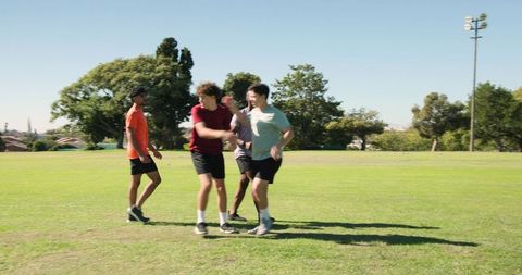 Young men sprinting and celebrating on green sports field during outdoor fitness training