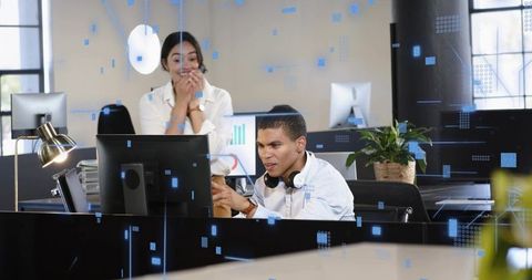 Team collaborating at workstation with digital UI overlays, man pointing at monitor
