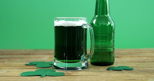 Green beer in a clear mug next to a green bottle on a wooden table with green shamrock decorations, set against a green background. Suitable for St. Patrick's Day promotions, festive events, Irish-themed parties, and holiday advertisements.