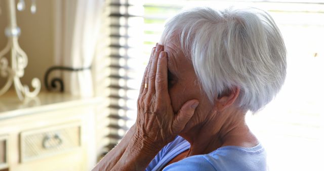 Stressed senior woman covering her face with hands at home