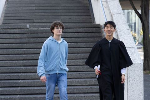 College friends walking campus steps celebrating graduation with diploma and joyful smile