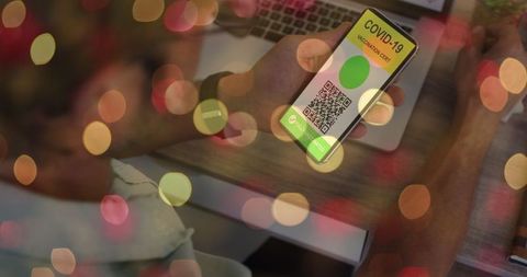 Man holding smartphone with covid-19 vaccine passport amid bokeh lights