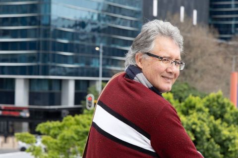 Senior man standing on city balcony smiling while overlooking skyline in maroon sweater