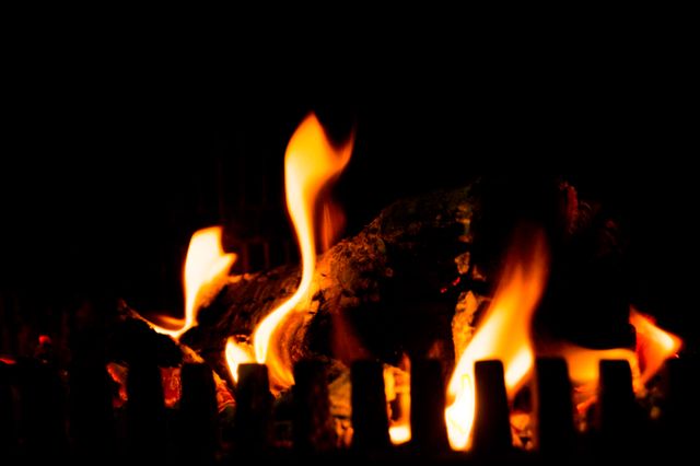 Burning firewood creating warm and cozy atmosphere at night. Perfect for use in articles and advertisements about home heating, winter comfort, relaxation, and rustic settings.