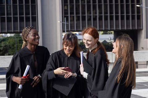 Diverse female graduates celebrating on urban terrace holding diplomas and mortarboards