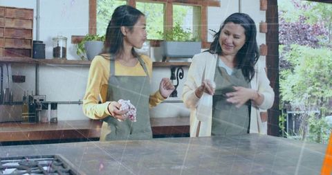 Two women chatting and preparing food in bright home kitchen with garden view
