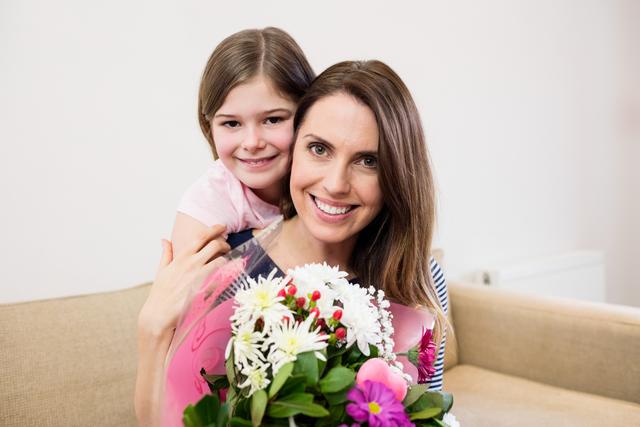 Image shows a mother receiving a bouquet of flowers from her daughter in a living room. Both are smiling, portraying a joyful and loving moment. Suitable for use in family-themed promotions, Mother’s Day campaigns, parenting blogs, or celebratory event advertisements.