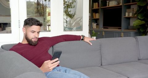 Man Relaxing on Grey Sofa Using Smartphone in Minimalistic Living Room