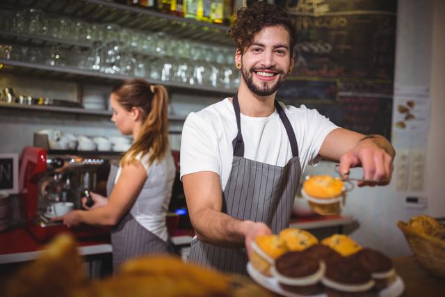 Portrait of waiter holding a plate of cup cake at counter in cafÃ©