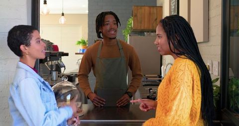African american barista serving customers at coffee shop counter using tablet and pastry display