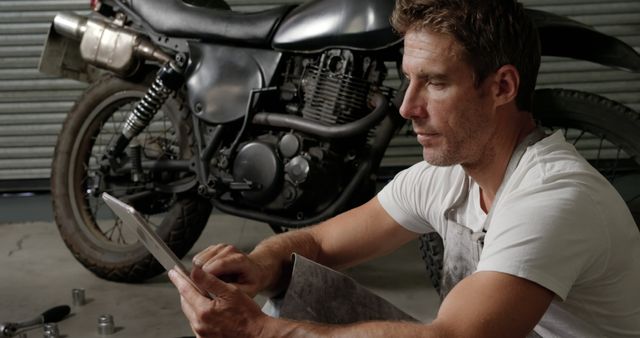 Man Repairing Motorcycle in Workshop Sitting with Tablet - Download Free Stock Images Pikwizard.com