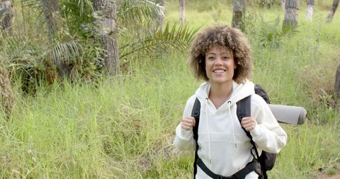 Happy woman hiking in grassy woodland with backpack
