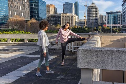 Rooftop women stretching for workout with city skyline, outdoor fitness and wellness