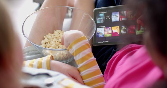 Family gathered with a tablet, bowl of popcorn, enjoying movie night. Perfect for content on family bonding, cozy indoor activities, entertainment at home, and nostalgia of childhood movie nights.