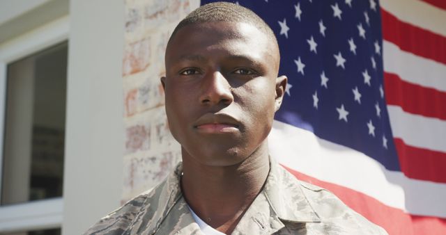 Depicting African American soldier in uniform standing proudly in front of an American flag. Ideal for themes of patriotism, military service, national defense, and honoring veterans' dedication.