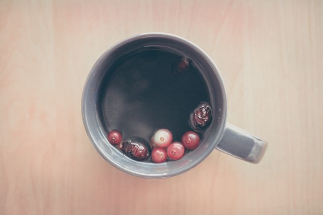 Overhead view of a ceramic cup filled with herbal tea, featuring cranberries floating on the surface. Ideal for promoting calmness and relaxation, this image is perfect for use in blogs about health and wellness, recipe websites, or social media posts advertising cozy home decor or specialty drinks.