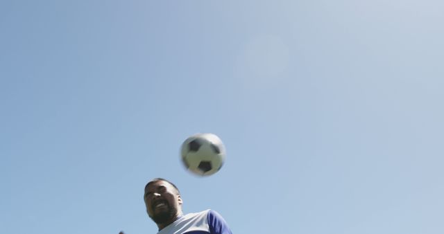 Biracial male football player playing match, heading ball on outdoor pitch. Football, sports and fitness.