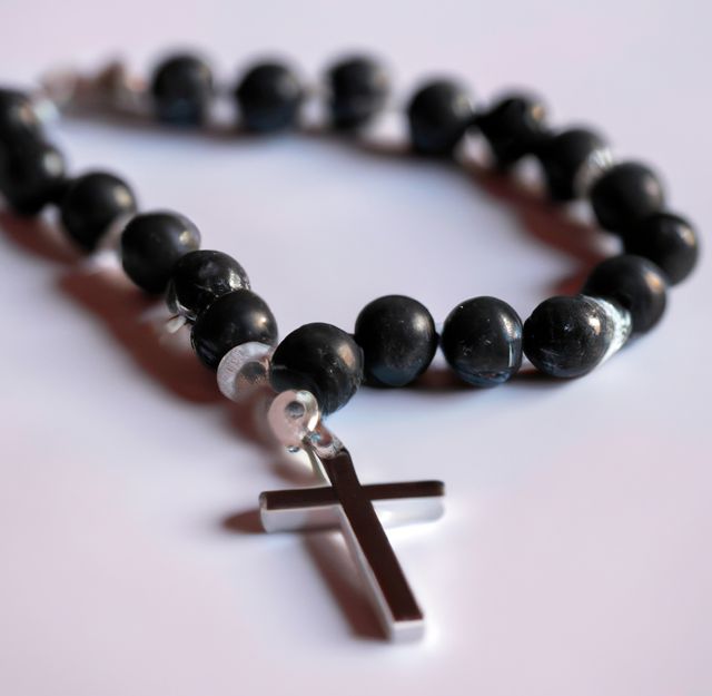 Close up of black rosary with cross on white background. Religion, faith and prayer concept.