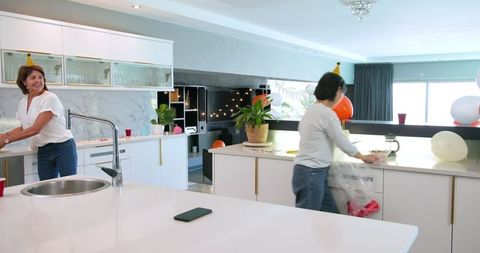 Senior Female Friends Cleaning Kitchen After Birthday Celebration