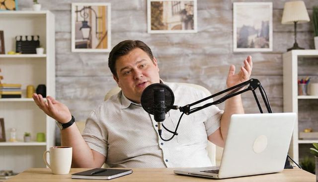Casual podcaster hosting engaging conversation at home desk with microphone and laptop