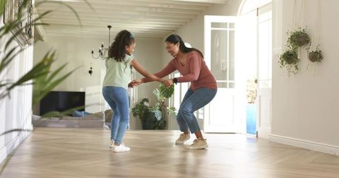African american mother and daughter playfully dancing on sunlit wood floor near open door