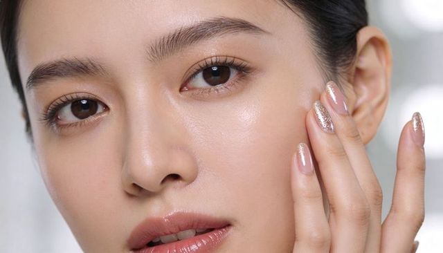 Asian woman touching cheek, dewy luminous skin with glossy lips and glitter manicure
