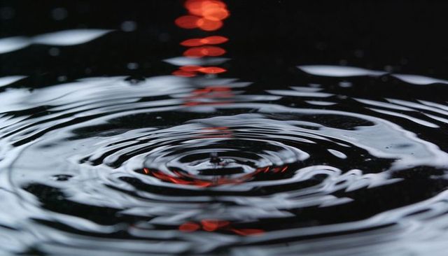 Dark water ripples with concentric droplet rings and red bokeh reflection abstract close-up