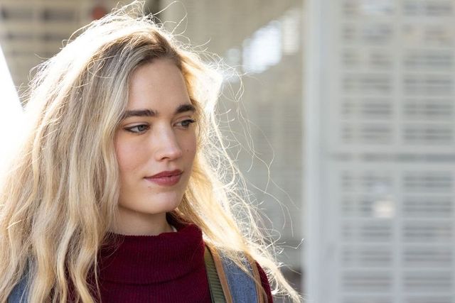 Backlit young woman commuter standing in sunlit city portrait wearing burgundy turtleneck