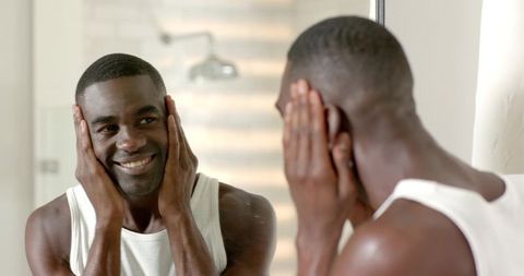 African american man smiling at mirror practicing morning grooming and skincare routine
