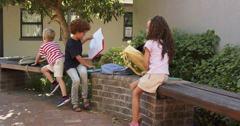 Schoolchildren unpacking backpacks on courtyard bench, playful after-school break