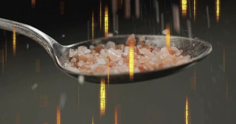 Himalayan pink salt crystals on spoon with golden light streaks, closeup texture