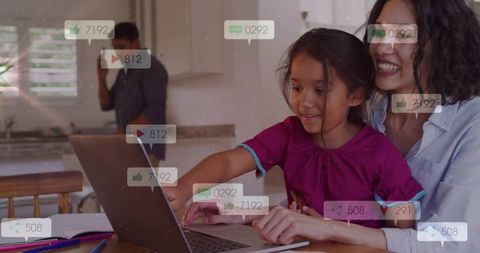 Mother guiding daughter using laptop at kitchen table, learning together, digital family