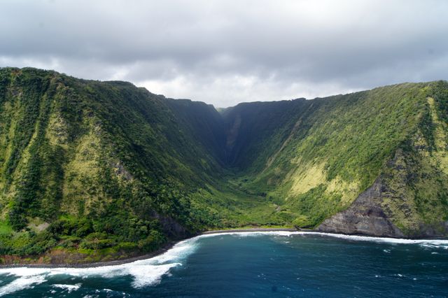 A stunning image of a verdant valley surrounded by steep green mountains leading to the sea coast. The deep azure waves crash gently against the shoreline while the vibrant tropical greenery flourishes. Perfect for travel advertisements, nature blogs, environmental presentations, and scenic calendars showcasing breathtaking natural landscapes.