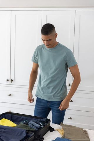 Young man packing suitcase on bed in minimalist bedroom preparing weekend travel plans