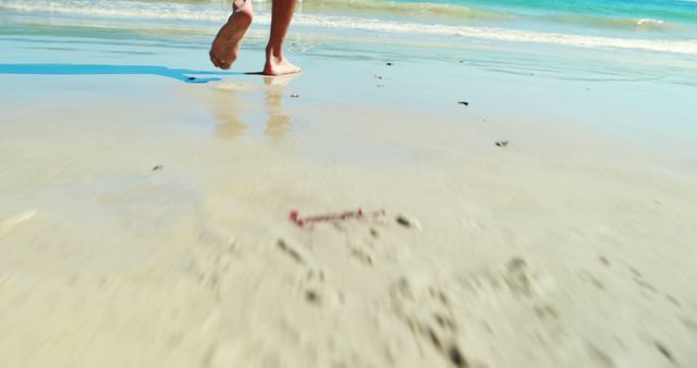 Person's feet walking barefoot on sandy beach near the sea. Clean beach with clear blue water, calm and relaxing atmosphere. Ideal for vacation promotions, travel blogs, outdoor lifestyle content, or nature-related themes.
