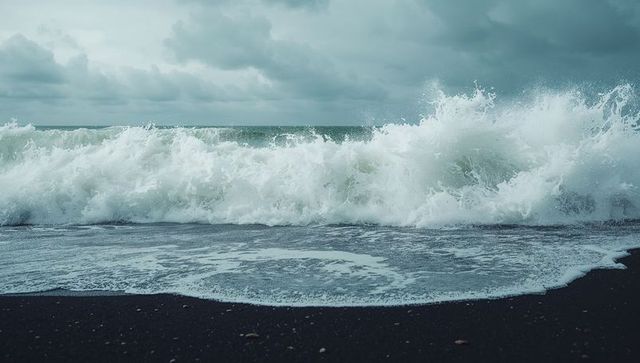 Crashing ocean waves on wet black sand beach with foamy surf and stormy grey sky