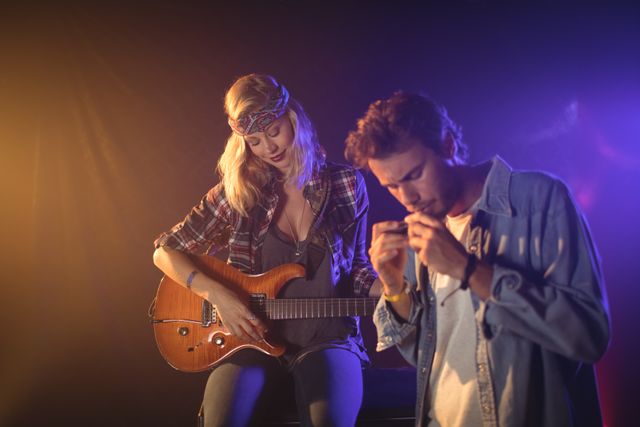 Female guitarist and male harmonica player performing together on stage in a nightclub. Ideal for use in articles or promotions related to live music events, nightlife entertainment, musical performances, and artistic collaborations.