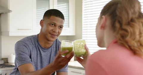 Couple toasting green smoothies at kitchen counter during morning wellness ritual