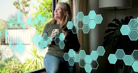 Senior woman sipping coffee on sunny window sill with augmented reality hexagon overlays